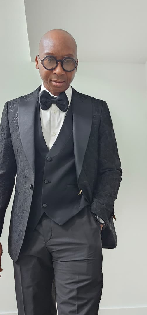 Man wearing a black tuxedo with a white shirt and bow tie against a plain background