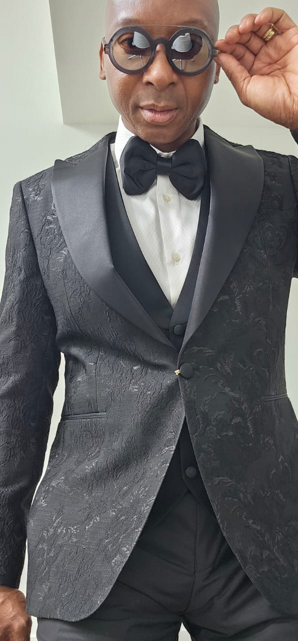 Man wearing a black tuxedo with a bow tie against a plain background