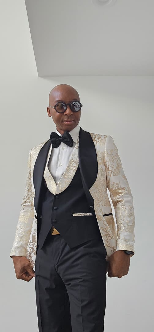 Man wearing a formal black and Gold Tuxedo with a bow tie against a plain background