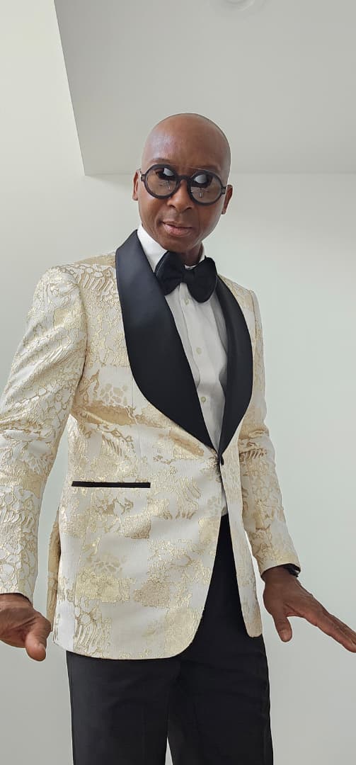 Man wearing a gold tuxedo with black lapels and bow tie against a plain background