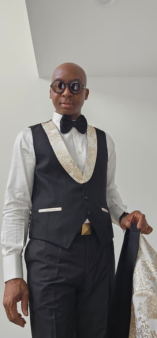 Man wearing a gold tuxedo with black lapels and bow tie against a plain background