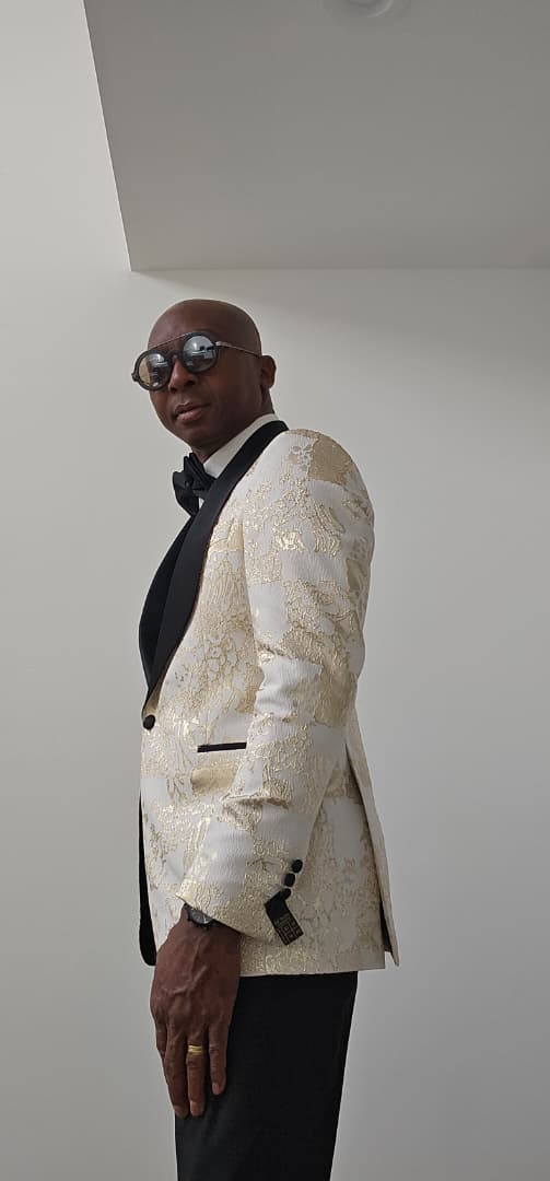 Man wearing a black and Gold Tuxedo against a plain background
