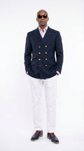 Man wearing a navy blazer with gold buttons, white shirt, and white pants on a white background