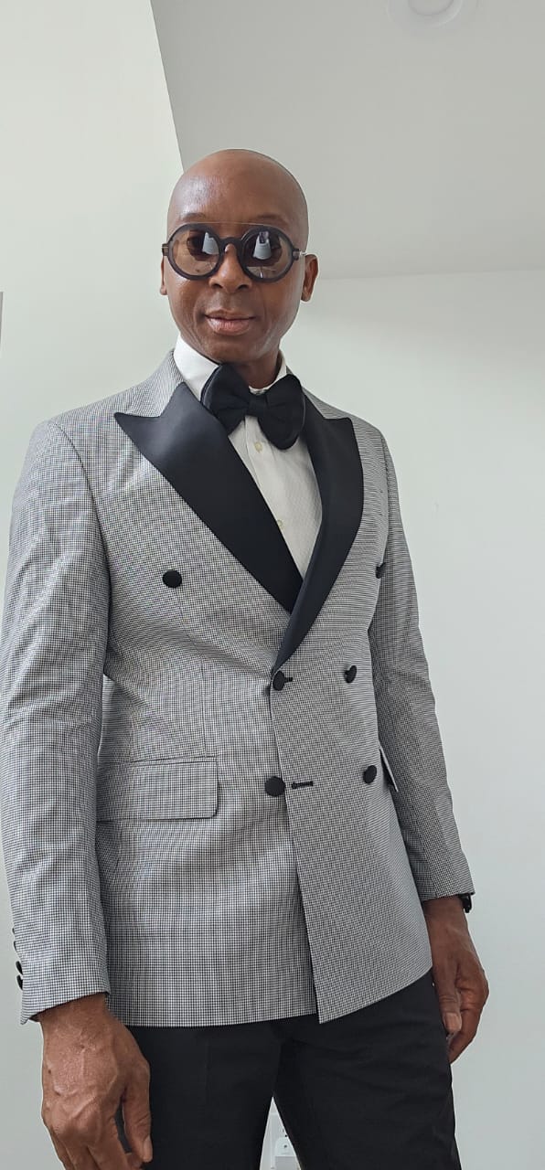 Man wearing a gray checkered suit with black lapels and bow tie against a white background