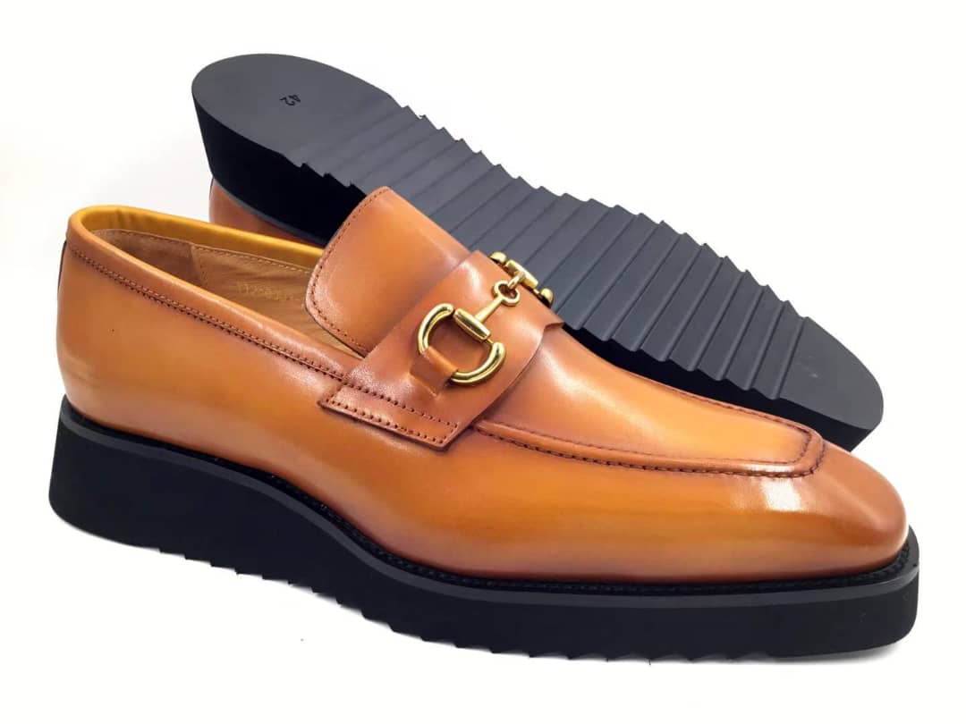 Brown loafer shoe with gold buckle on a white background