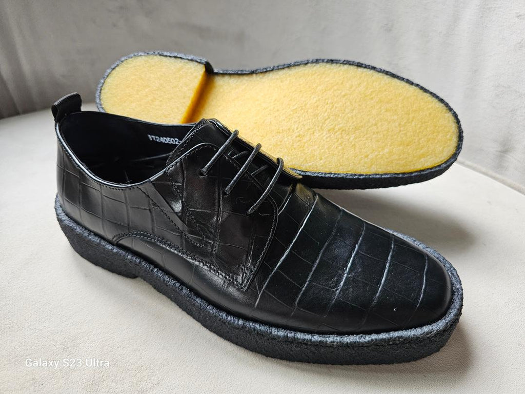 Black leather shoe with yellow insole on a light gray background
