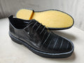 Black leather shoe with yellow insole on a light gray background