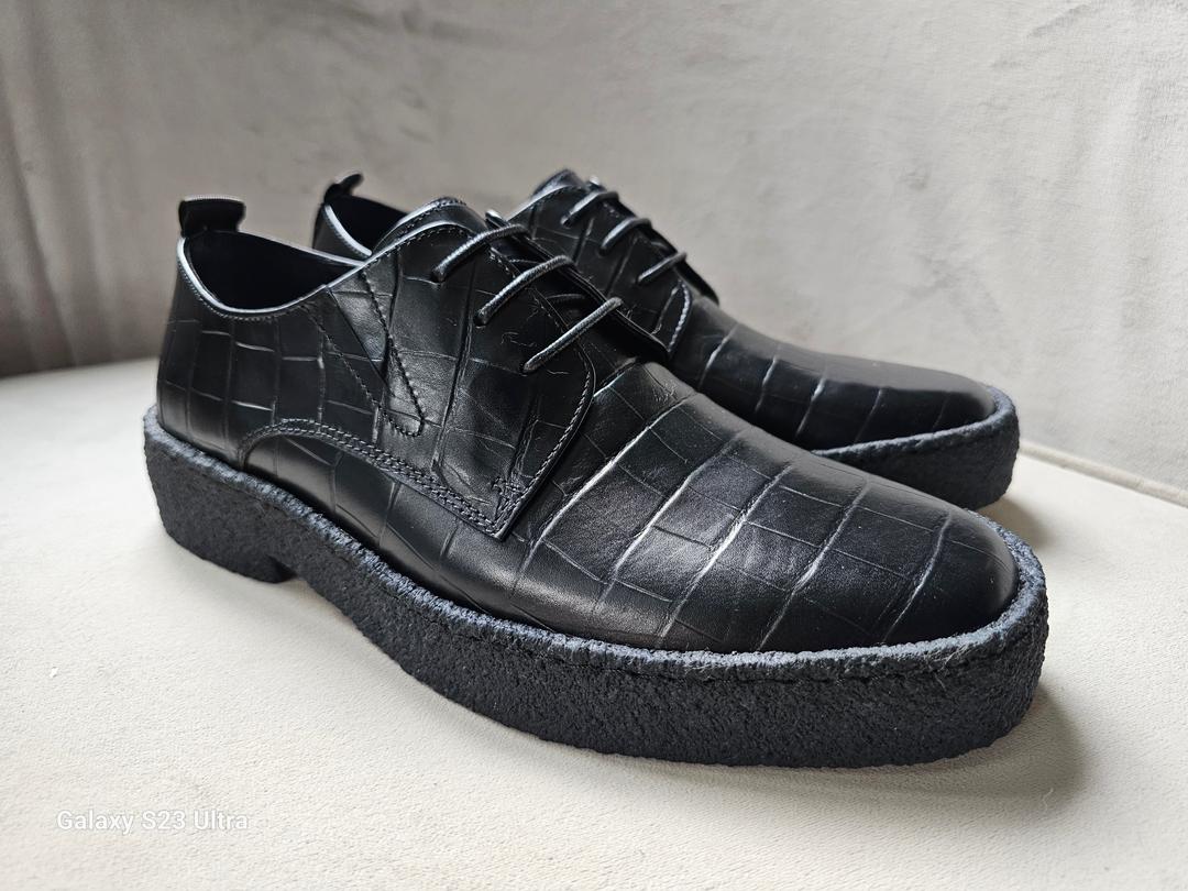 Pair of black leather shoes with textured sole on a light background