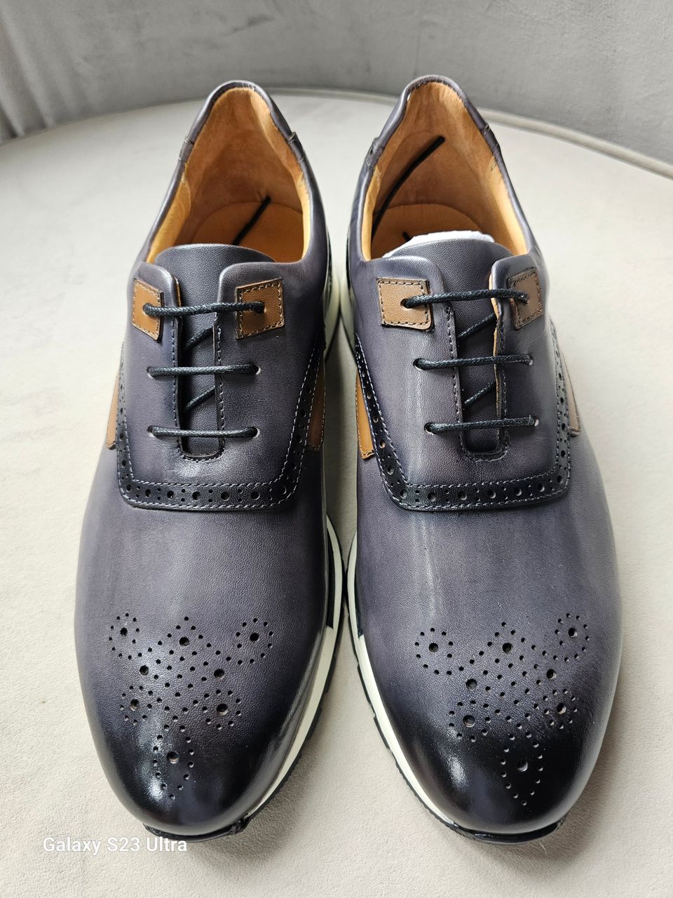 Pair of gray leather shoes with brown accents on a light surface