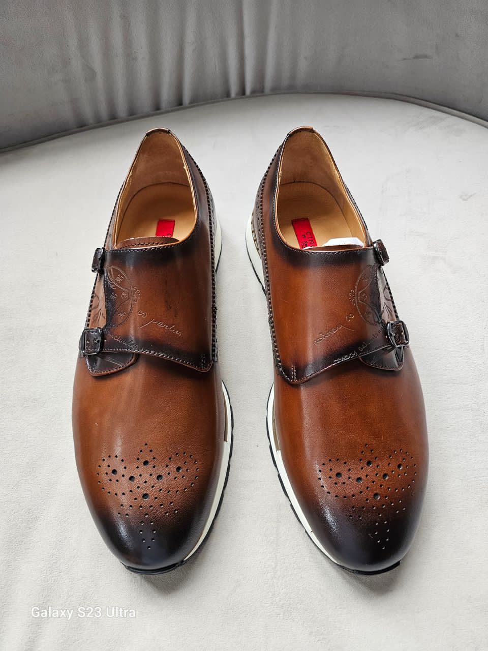 Pair of brown dress shoes with black soles on a light gray surface