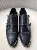 Pair of black leather shoes with buckles on a light gray surface