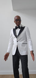 Man wearing a white tuxedo with black lapels and bow tie against a plain background