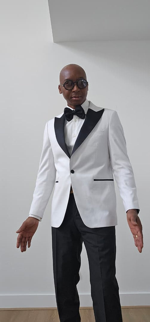 Man wearing a white tuxedo with black lapels and bow tie against a plain background