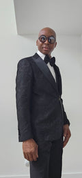 Man wearing a black tuxedo with a bow tie against a plain background