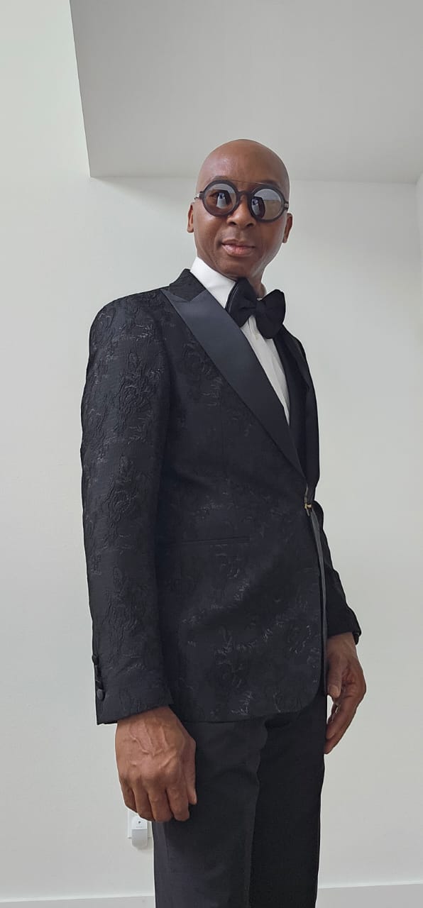 Man wearing a black tuxedo with a bow tie against a plain background