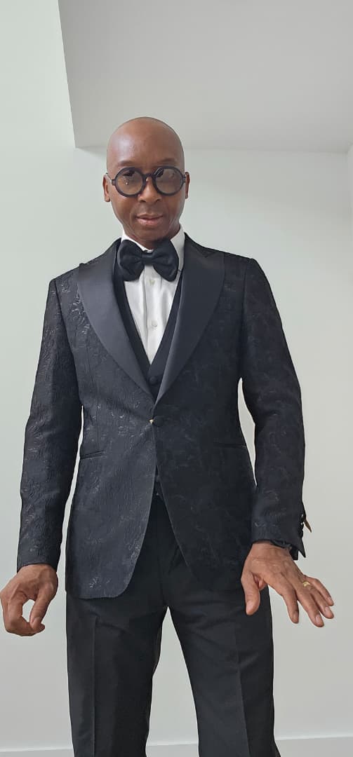 Man wearing a black tuxedo with a bow tie against a plain background